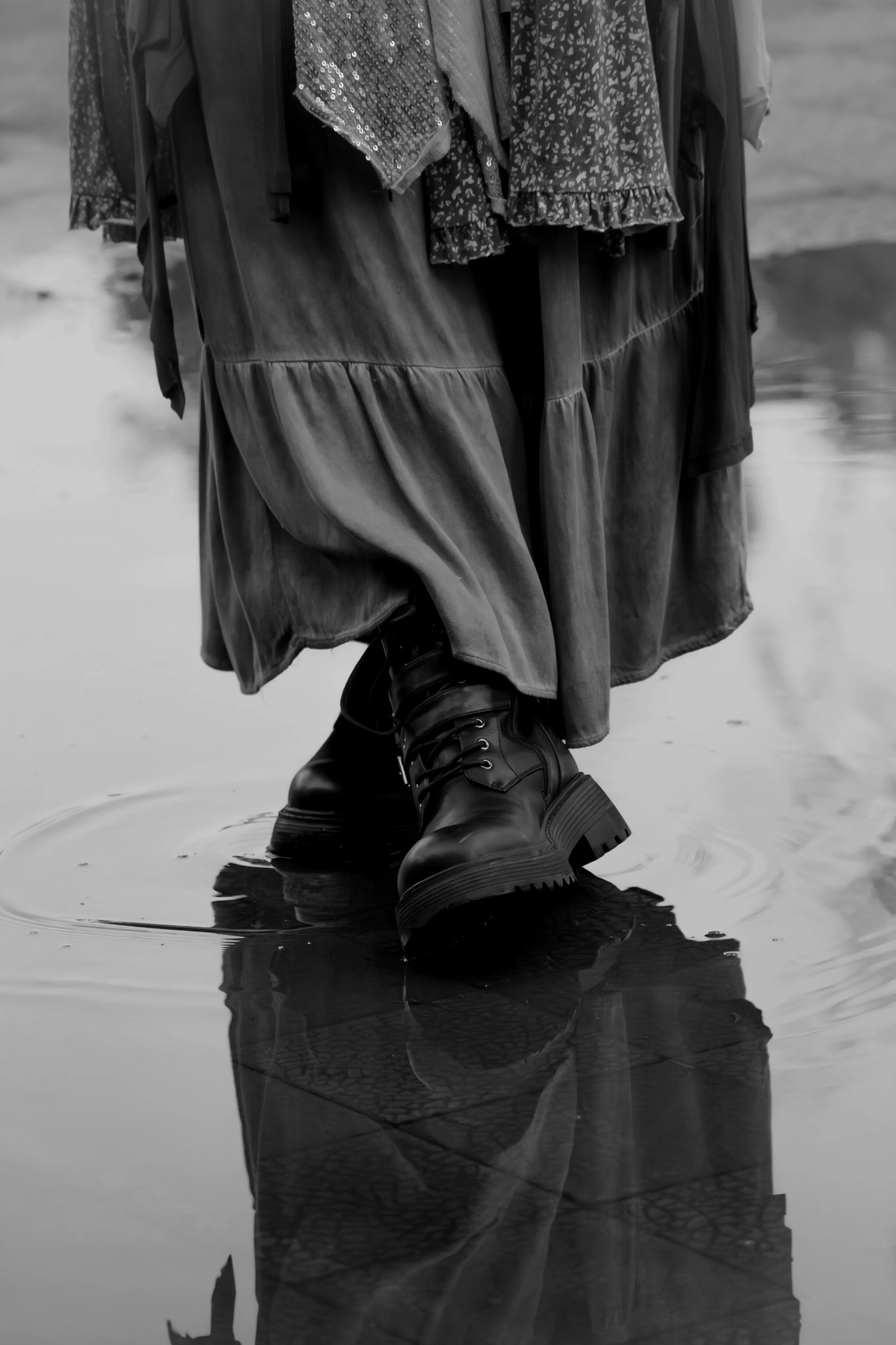 Botas negras sobre un charco reflejante, con una falda ondeando encima