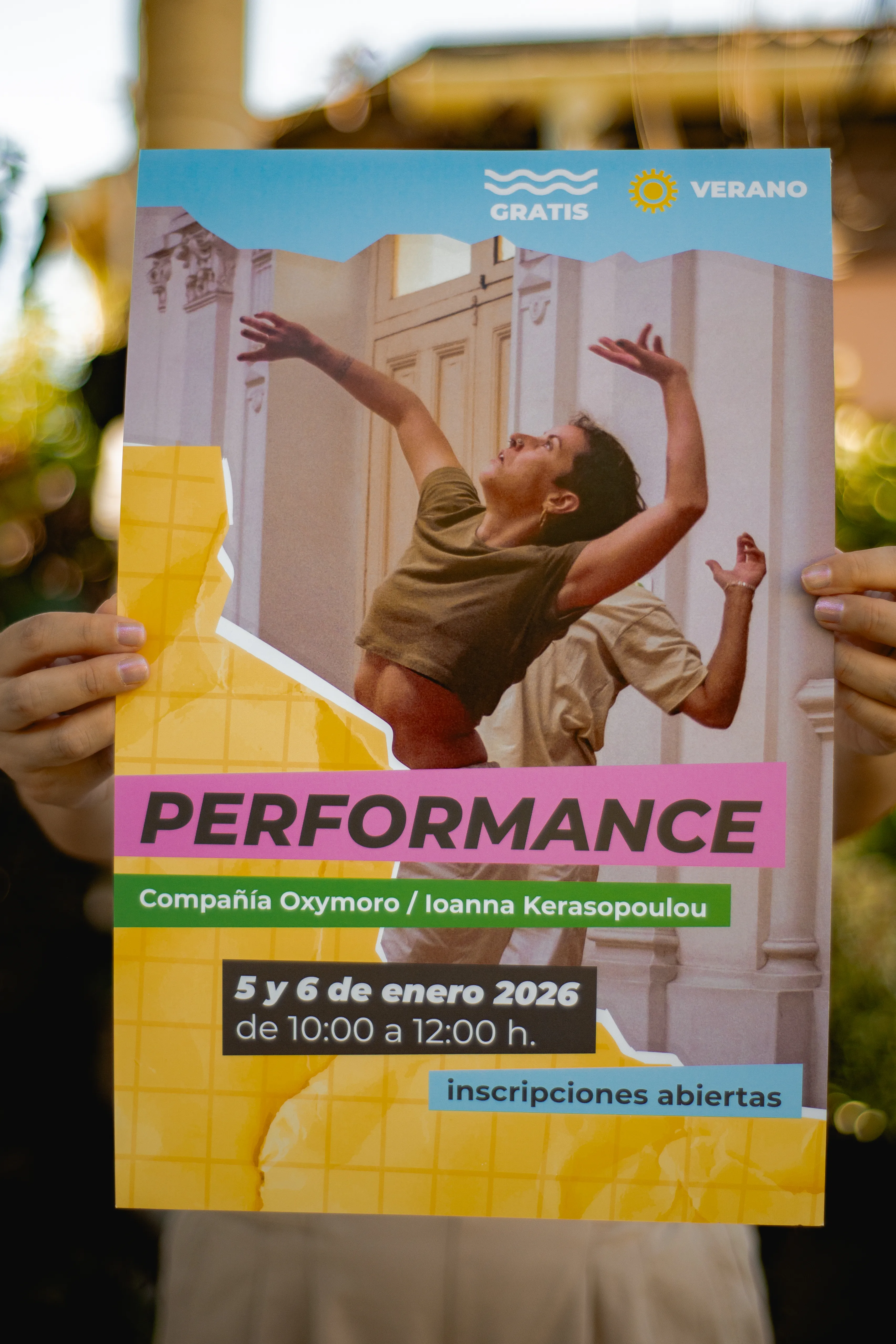 Persona sosteniendo el afiche amarillo del taller de Performance de los Talleres Intensivos de Verano de BAJ